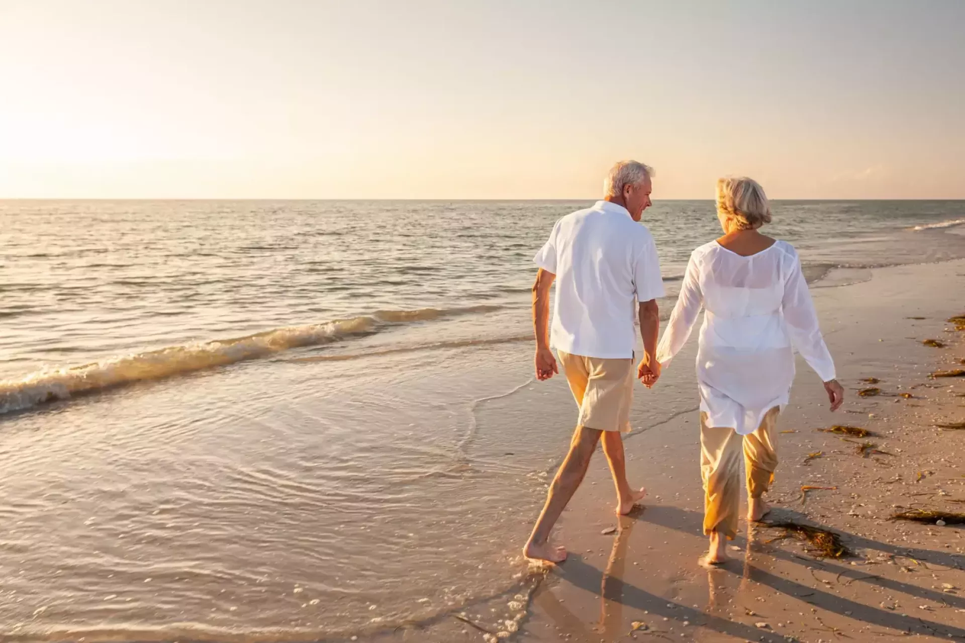 Ouder echtpaar hand in hand wandelend langs het strand bij zonsondergang.